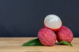 Three lychees, one cut open to reveal the white interior, placed on a wooden surface with green leaves.
