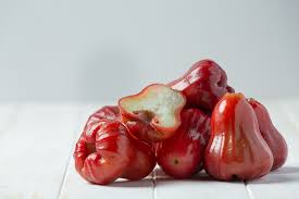 A pile of rose apples, some whole and others partially eaten, resting on a white surface.