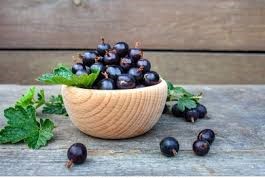 A light brown bowel full of jostaberries black color with green leave wooden wall background bowel on marbel table some berries felt on the table