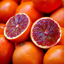A pile of bright orange blood oranges, with two fruits cut in half to reveal their deep red, juicy interiors, set against a blurred background.