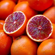 A pile of bright orange blood oranges, with two fruits cut in half to reveal their deep red, juicy interiors, set against a blurred background.
