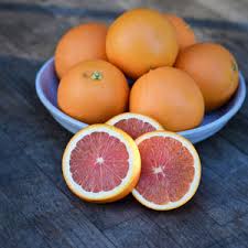 A shallow bowl filled with whole Cara Cara oranges, with two halves and a quarter of the fruit sliced open to reveal the deep pinkish-red flesh, placed on a wooden surface.