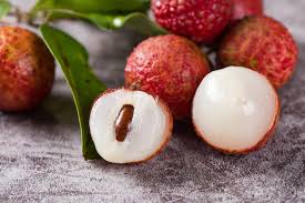image showing lychee fruits five peace one is full peeled and other one is half centre a seed on fruit some green leaves on the counter